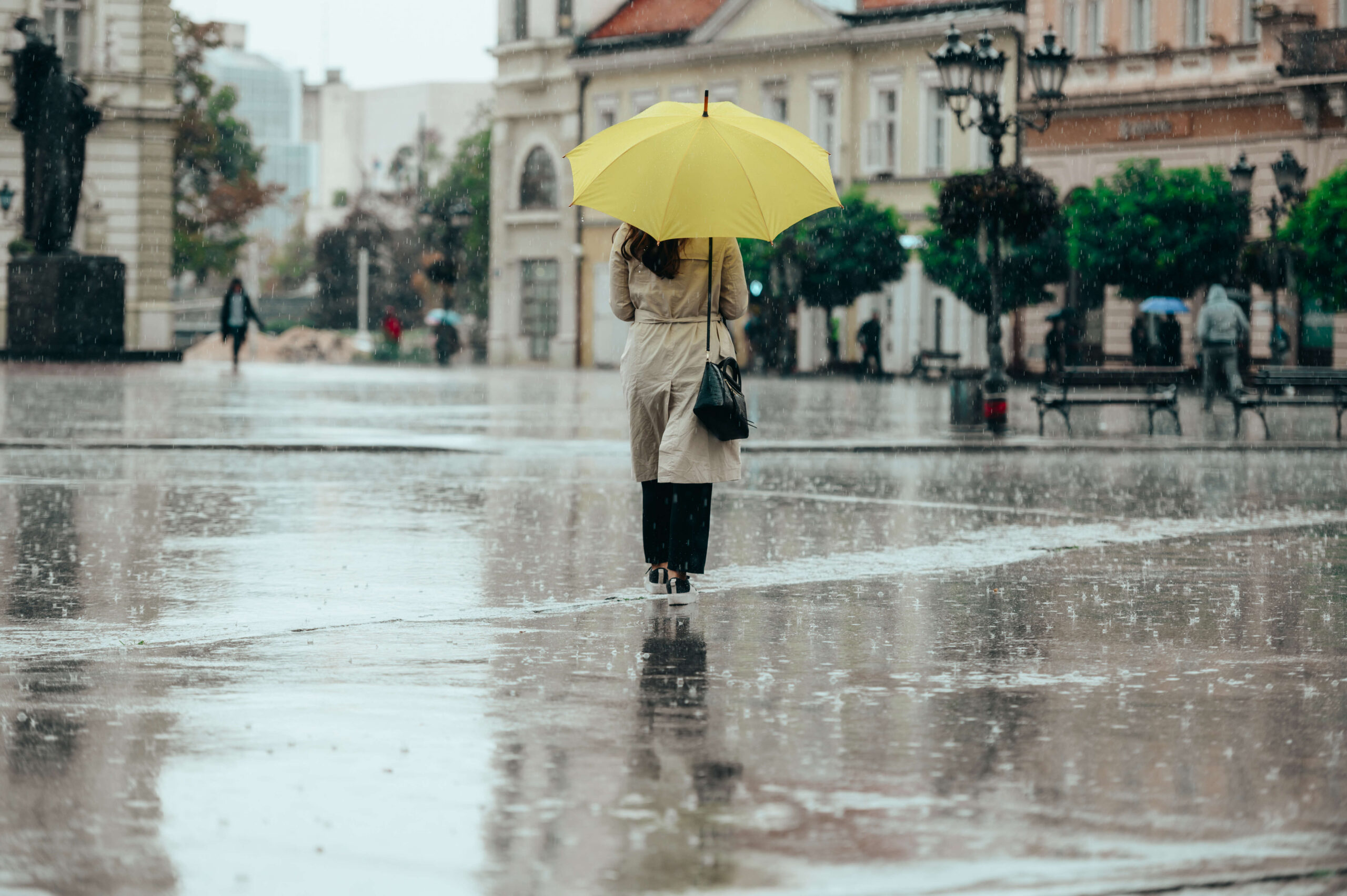 Kobieta z żółtym parasolem podczas intensywnego deszczu w mieście
