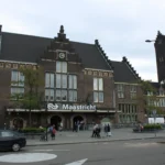 Budynek dworca kolejowego Maastricht z charakterystyczną wieżą zegarową i wejściem głównym.