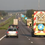 Roboty drogowe na holenderskiej autostradzie A58. Samochody mijają pojazd służb drogowych z tablicą kierującą ruch na lewy pas.