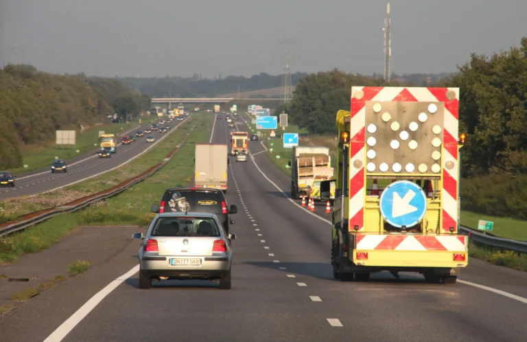 Roboty drogowe na holenderskiej autostradzie A58. Samochody mijają pojazd służb drogowych z tablicą kierującą ruch na lewy pas.