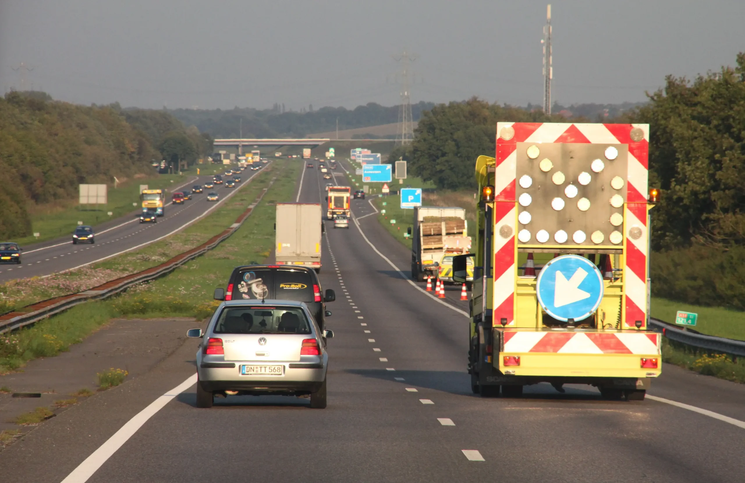 Roboty drogowe na holenderskiej autostradzie A58. Samochody mijają pojazd służb drogowych z tablicą kierującą ruch na lewy pas.