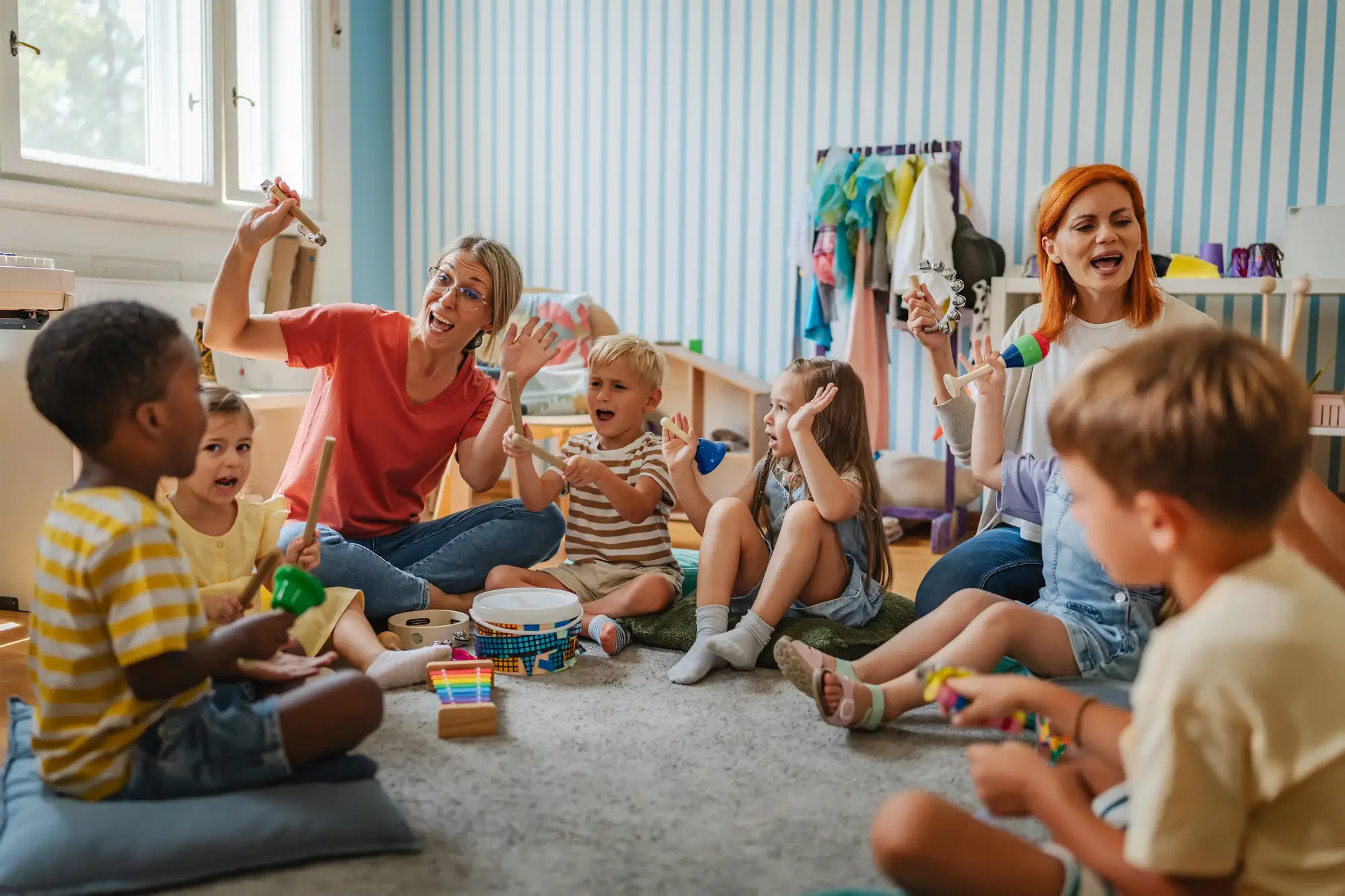 Opiekunki bawią się z grupą dzieci w kolorowej sali przedszkolnej.