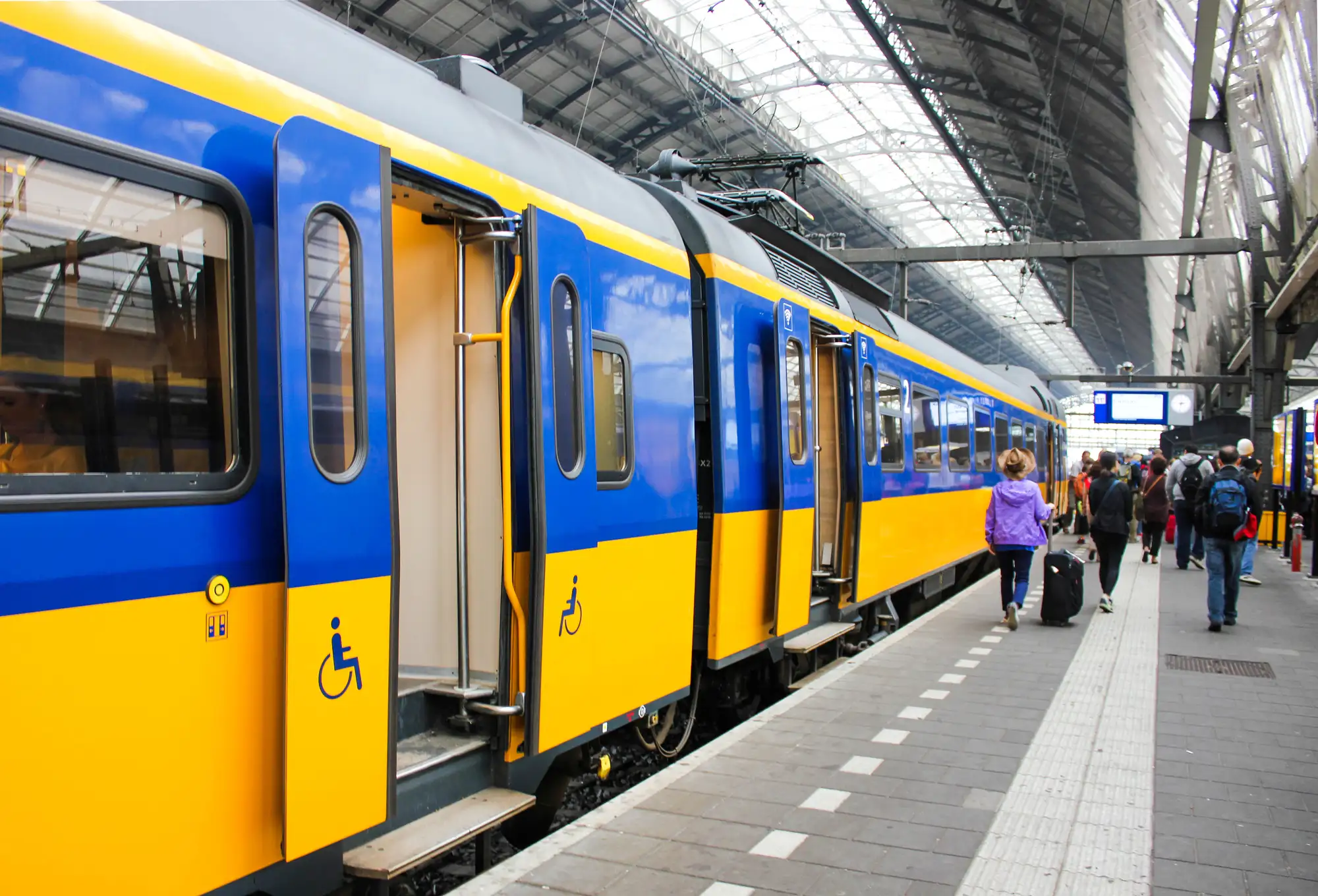 Żółto-niebieski pociąg NS przy peronie na stacji w Holandii, pasażerowie wchodzący do pociągu