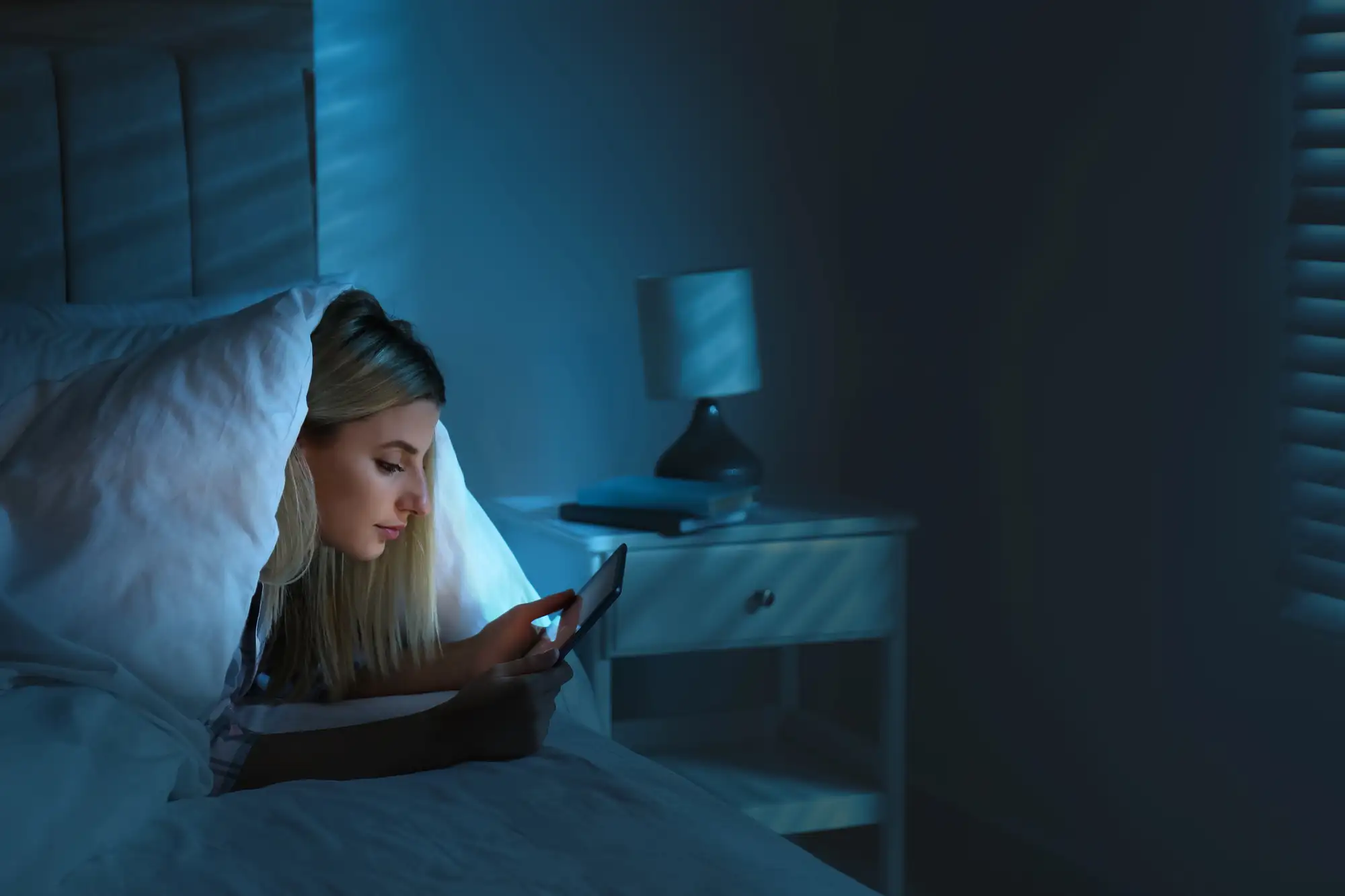 Młoda kobieta korzystająca ze smartfona w łóżku w nocy