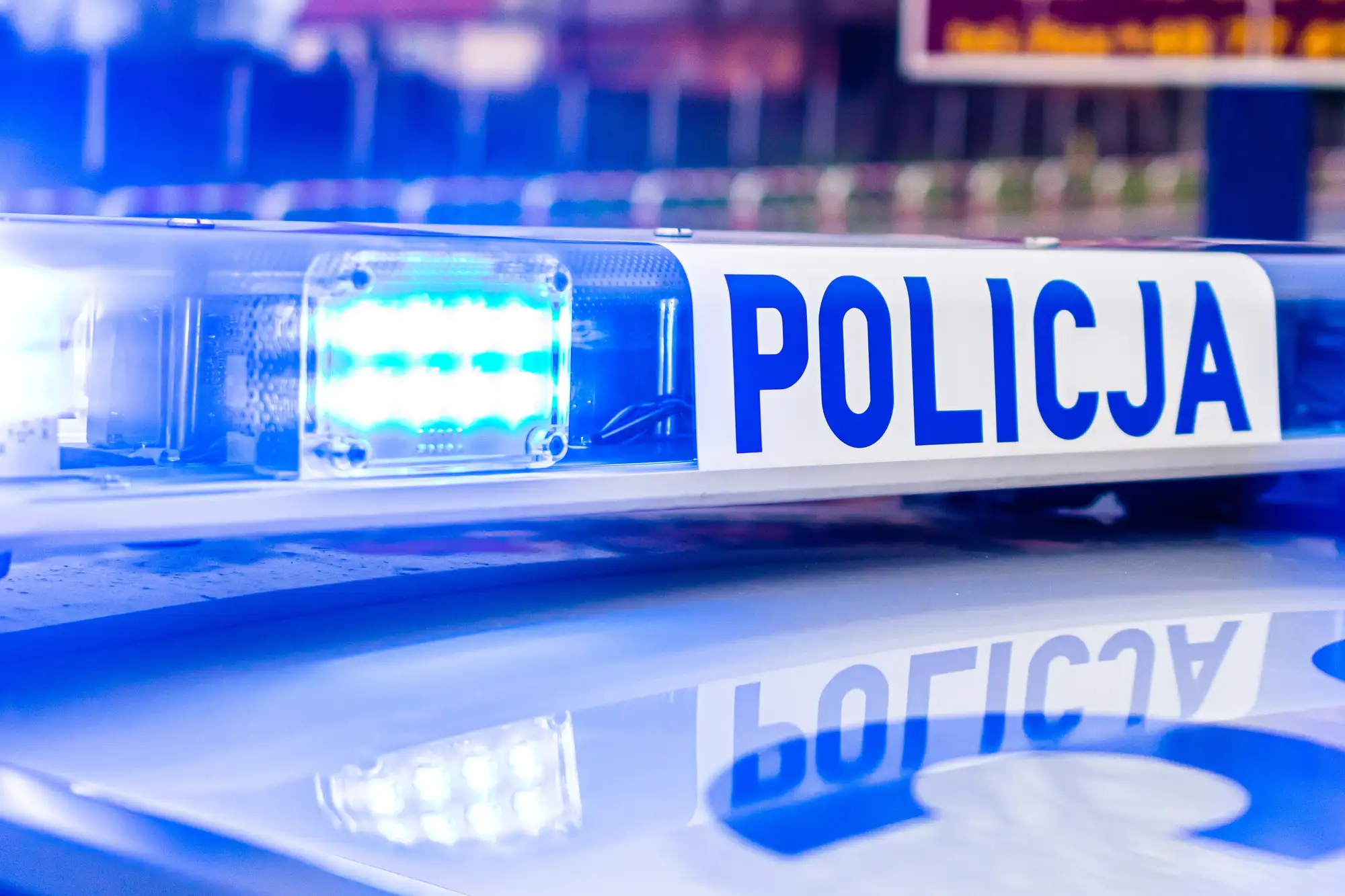 Niebieskie światła radiowozu polskiej policji i napis POLICJA na belce sygnalizacyjnej.