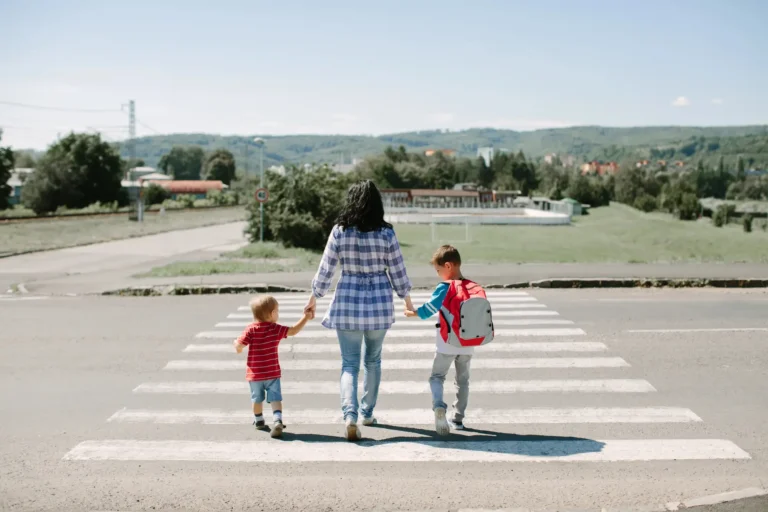 Mama prowadząca za ręce dwoje dzieci z plecakami na ścieżce wśród zieleni
